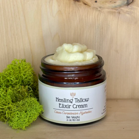 A jar of Healing Tallow Elixir Cream with a label on the front, placed on a wooden surface, with a piece of green moss to the left.