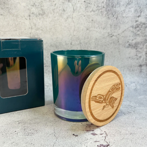 A white candle container with a black label that reads 'RavenSong' and 'FERN WOMAN'. The lid is off to the side, revealing a white candle inside.