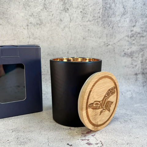 A white candle in a metal container with a label reading 'Sacred Smudge' on a light background.