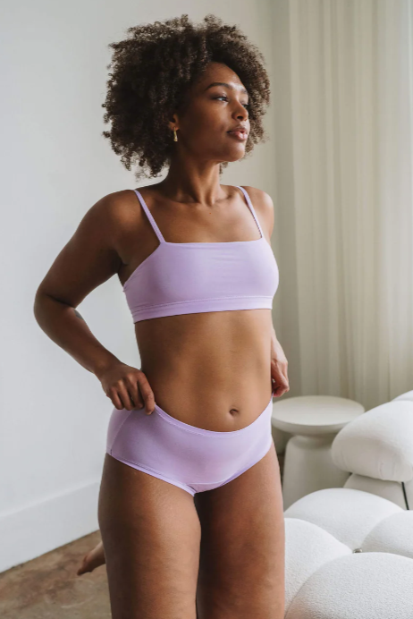 Woman wearing a light purple bikini set in a room with neutral decor.