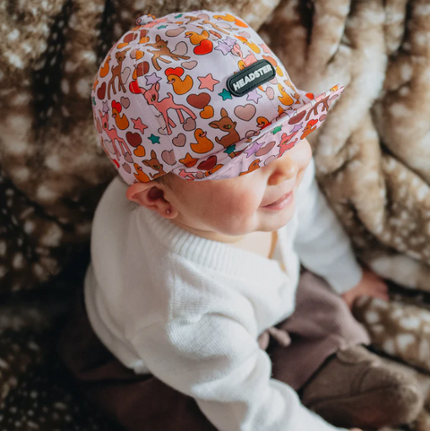 Baby wearing a colorful cap with animal patterns on a soft, patterned background