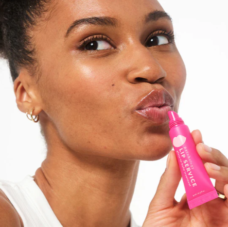 Woman applying pink lip balm labeled 'Lip Service' to her lips.