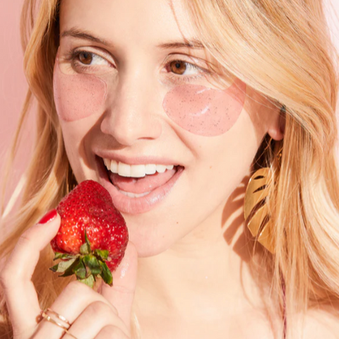 Woman holding a strawberry against a pink background