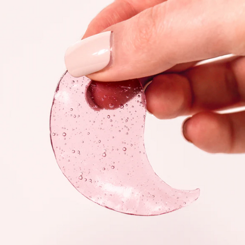Hand holding a pink crescent-shaped object with bubbles on a white background