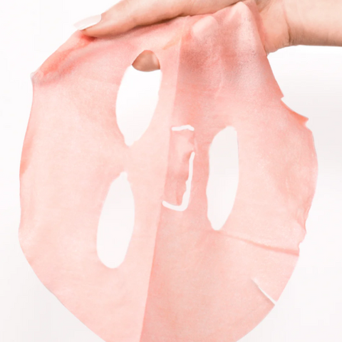 Pink face mask sheet held by a hand on a white background