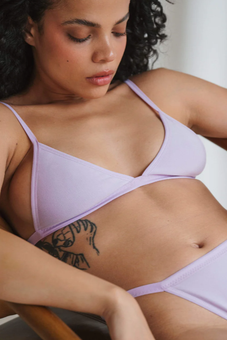 Woman wearing a light purple bra and panties set against a neutral background