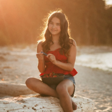 Woman sitting on a log by the beach with a blurred forest background