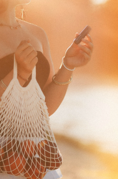 Person holding a phone and a white mesh bag with a warm, blurred background