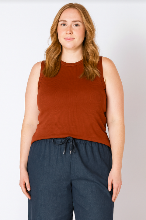 Woman wearing a rust-colored sleeveless top and dark blue pants against a plain background