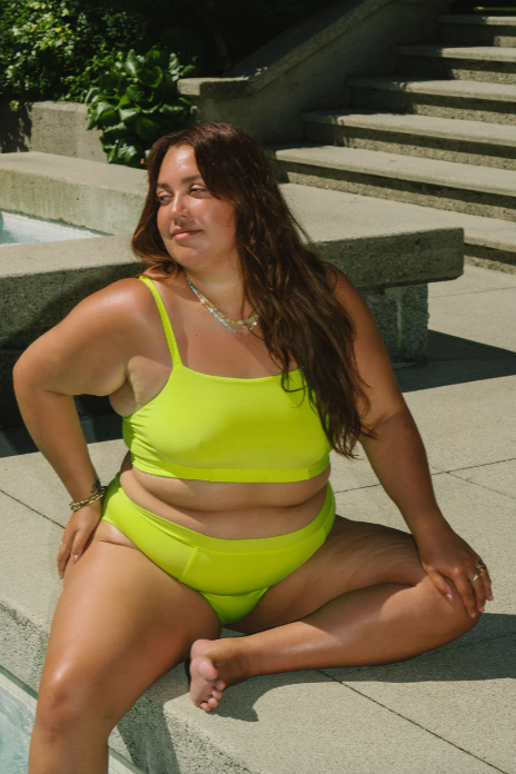 Woman in a bright green bikini sitting on stone steps outdoors