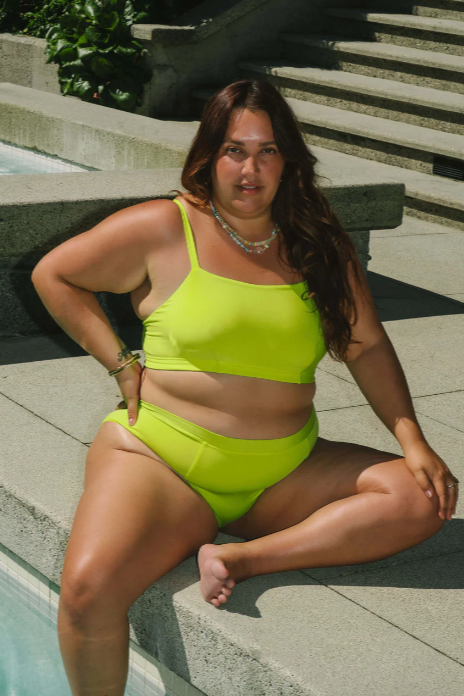 Woman in a bright green bikini sitting by a pool.
