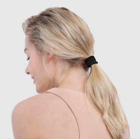 Woman with blonde hair tied in a ponytail with a black hair tie on a white background