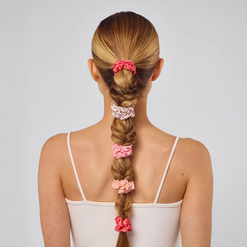 Woman with braided hair wearing pink scrunchies on a plain background
