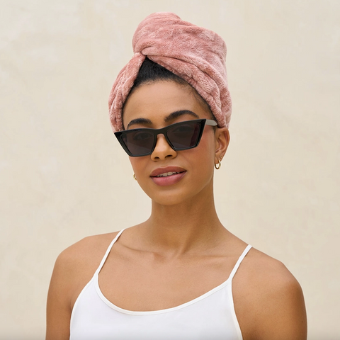 Woman wearing a pink towel on her head and sunglasses with a beige background