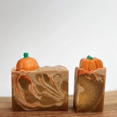 Two pumpkin-shaped soaps on a wooden block with a website interface in the background.