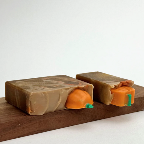 Two soap bars with pumpkin designs on a wooden board against a white background