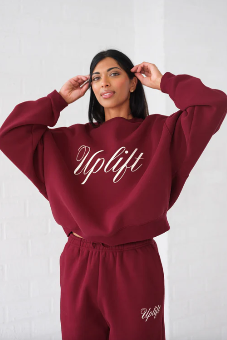 Person wearing a burgundy 'Uplift' sweatshirt and pants on a white background