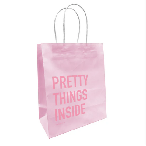A pink paper gift bag with 'PRETTY THINGS INSIDE' printed in capital letters on the side, featuring twisted paper handles.