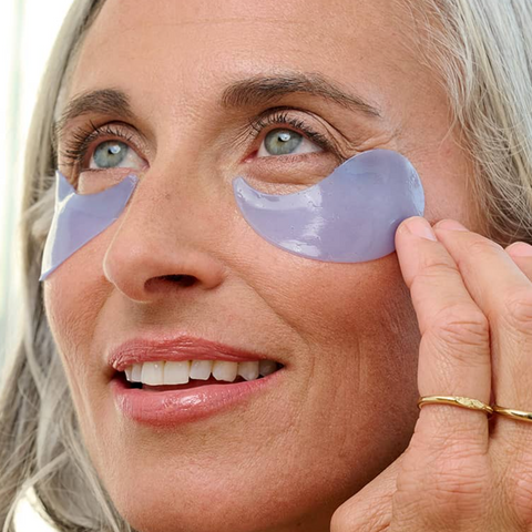 Woman applying purple eye patches to her eyes