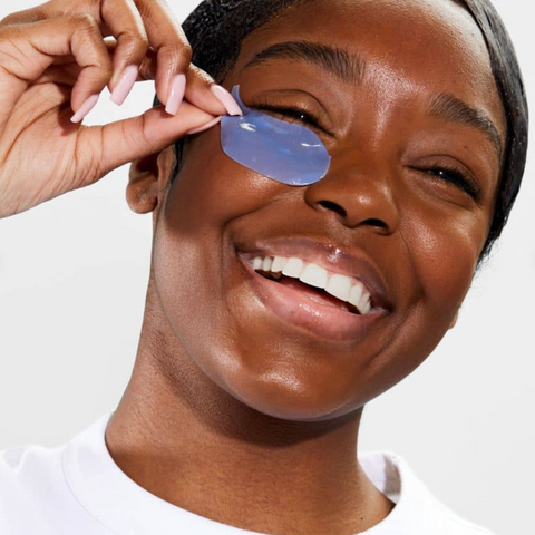 Person applying a blue eye mask to their eye with a hand
