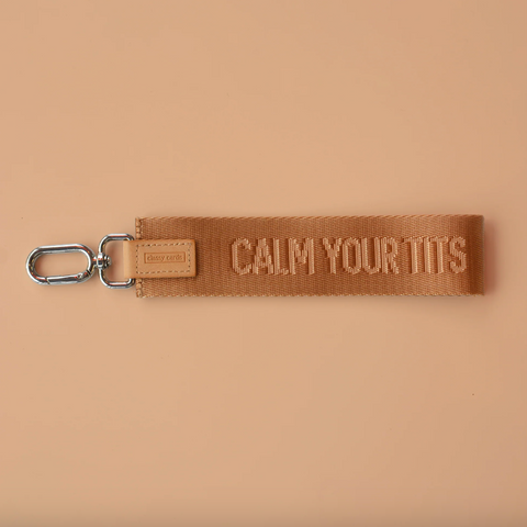 Brown woven keychain with 'CALM YOUR Tits' text on a beige background