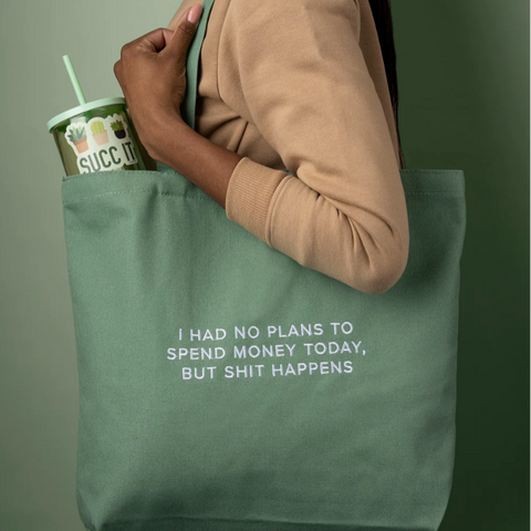 Person holding a green tote bag with a humorous quote, against a plain background