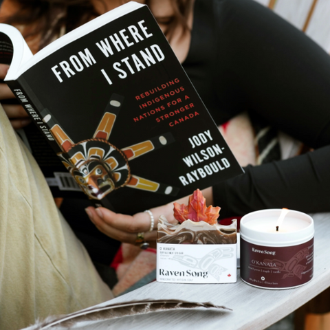 Woman reading a book titled 'From Where I Stand' with a candle and product on a table.