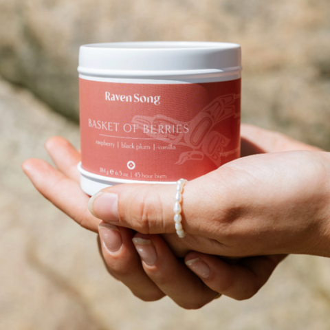 Hand holding a candle labeled 'Raven Song' with a blurred natural background