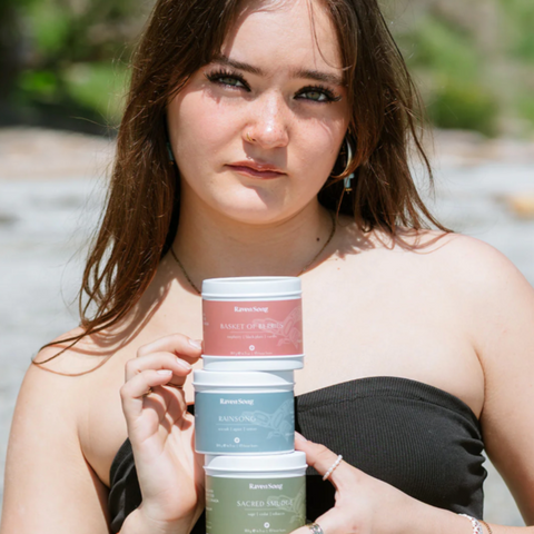 Woman holding three small containers outdoors with a blurred natural background