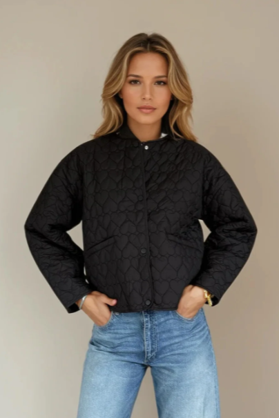 Woman wearing a black quilted jacket and blue jeans against a beige background