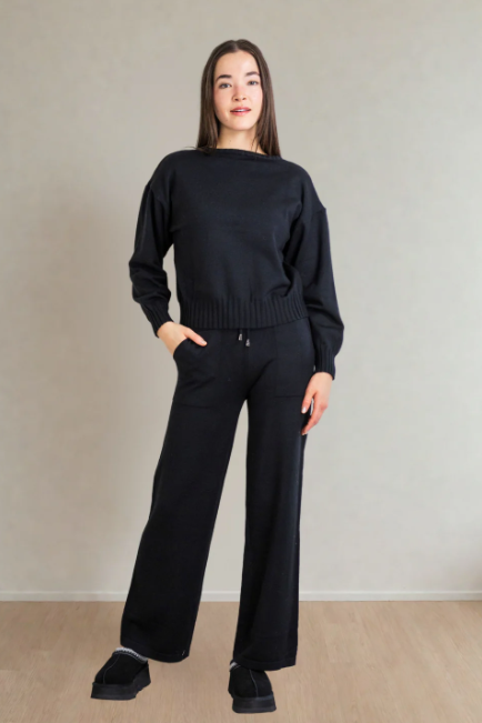 Person wearing a black sweater and pants against a plain background