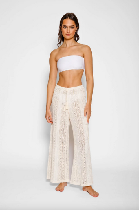 Woman wearing a white strapless top and beige wide-leg pants on a plain background