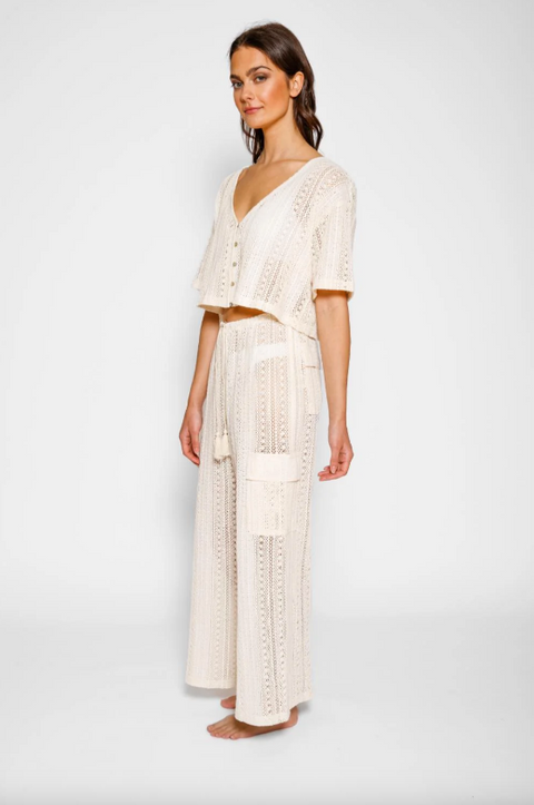 Woman wearing a white crochet outfit on a plain background