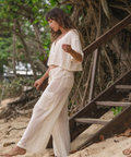 Woman in a white outfit standing on a sandy path with trees in the background