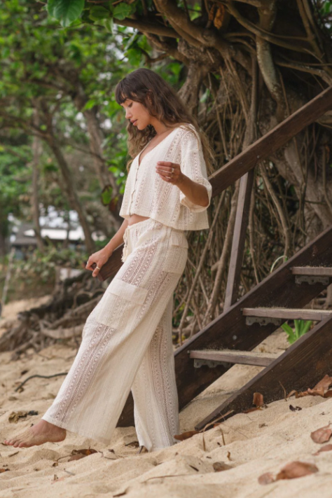 Woman in a white outfit standing on a sandy path with trees in the background