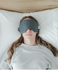 Person wearing a gray sleep mask lying on a bed.