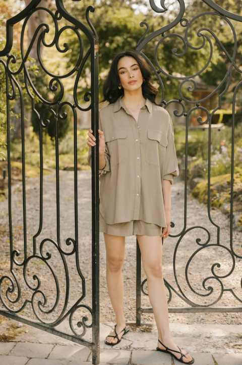 Woman in a beige outfit standing behind an ornate metal gate.
