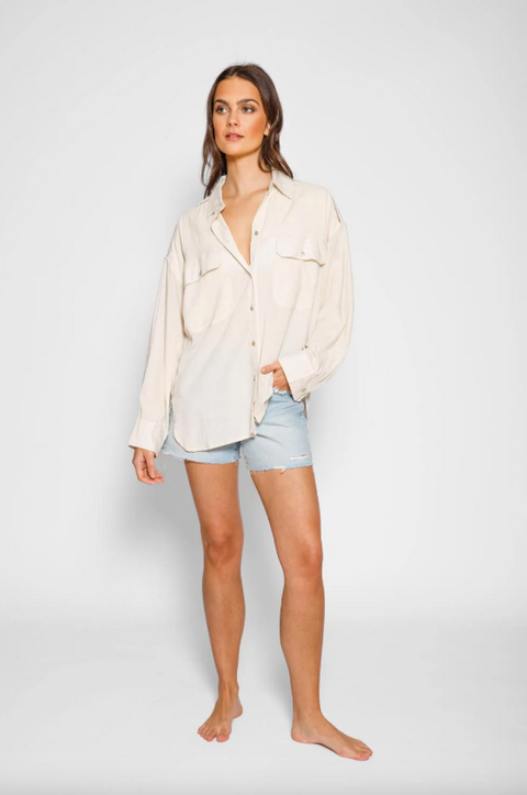 Woman wearing a light-colored shirt and denim shorts on a plain background