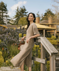 Woman in a beige dress standing on a wooden bridge in a garden setting