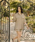 Woman in a beige outfit standing through an ornate metal gate with a garden background