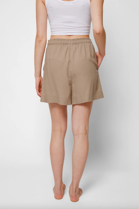 Person wearing beige shorts and a white top on a plain background