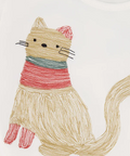 Close-up of a white crewneck top featuring a whimsical embroidered cat design wearing a red and teal striped sweater.