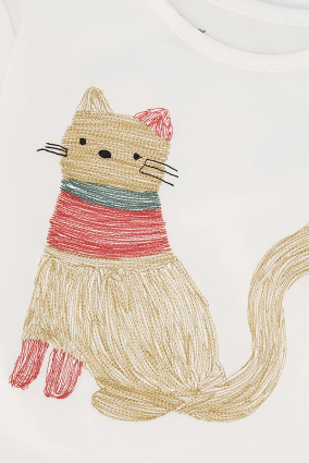 Close-up of a white crewneck top featuring a whimsical embroidered cat design wearing a red and teal striped sweater.