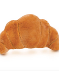 A plush croissant-shaped eye pillow in a warm golden-brown color, shown on a white webpage layout with the Fred logo and product details.
