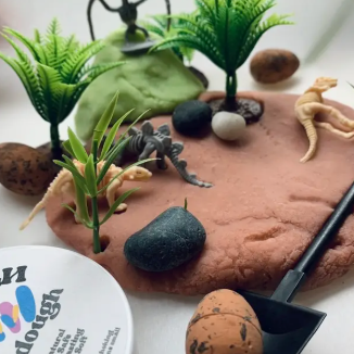 Play dough landscape with plants, rocks, and a tool on a white surface