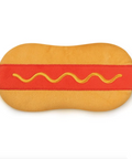 A hot dog-shaped plush cushion or pillow with a tan body, red sausage section, and yellow wavy line detail, shown on a white webpage background with a Fred logo and macOS dock visible.