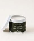 A white candle container with a black label that reads 'RavenSong' and 'FERN WOMAN'. The lid is off to the side, revealing a white candle inside.
