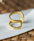 Gold ring with textured design on a white surface with a woven background