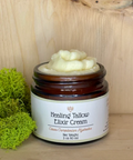 A jar of Healing Tallow Elixir Cream with a label on the front, placed on a wooden surface, with a piece of green moss to the left.