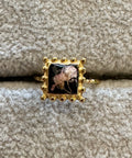 Gold ring with a black and white floral design on a textured beige surface